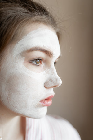 moisturizes the skin of the face with a white mask, nourishing cream for the skin of the face, portrait of a girl's curly planの写真素材