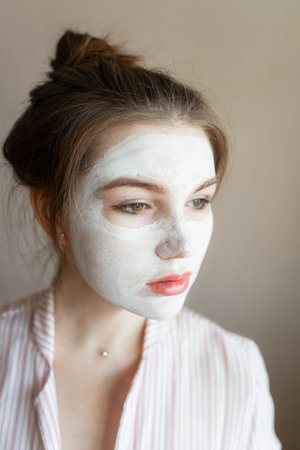 a girl with a clay mask on her skin looks into the distance, moisturizes her faceの写真素材