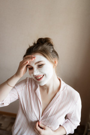 the girl laughs, takes care of the skin on her face, a white body mask, in a striped blouseの写真素材