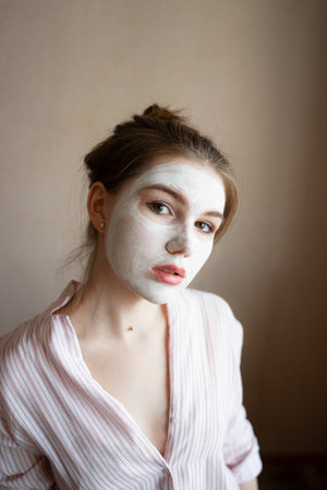 resting at home with a moisturizing white face mask, in a striped blouseの写真素材