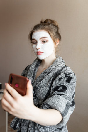 girl at home in kantha with a white mask on her face holds a phone in her handsの写真素材