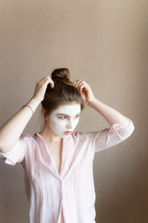 a girl with a moisturizer on her face looks away straightens her hair, in a blouse at homeの写真素材
