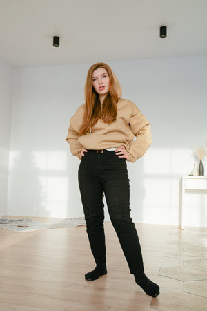 a full-length girl stands in the middle of the room looking at the camera in a brown hoodieの写真素材