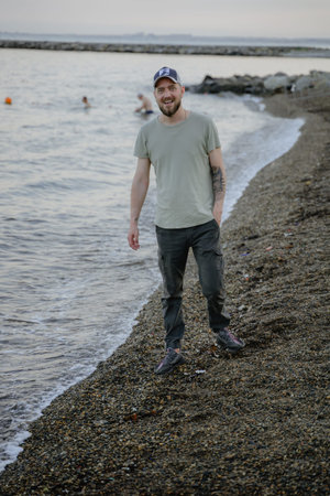 cheerful man with a beard walking along a pebble beach