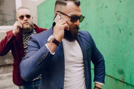Two bearded men use mobile phones outdoorsの写真素材