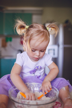 beautiful little girl learns to cook a meal in the kitchenの写真素材