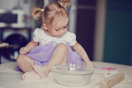beautiful little girl learns to cook a meal in the kitchenの写真素材