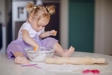 beautiful little girl learns to cook a meal in the kitchenの写真素材
