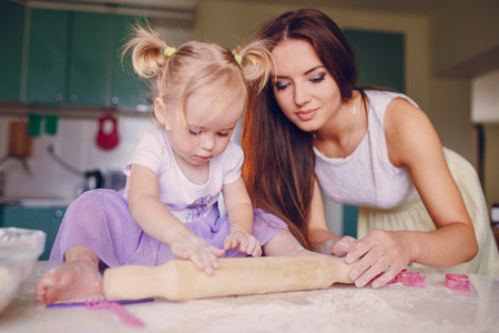 young beautiful mother teaches daughter prepare dough in the kitchenの写真素材