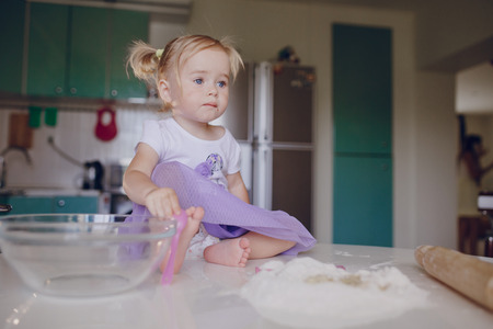 beautiful little girl learns to cook a meal in the kitchenの写真素材