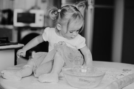 beautiful little girl learns to cook a meal in the kitchenの写真素材