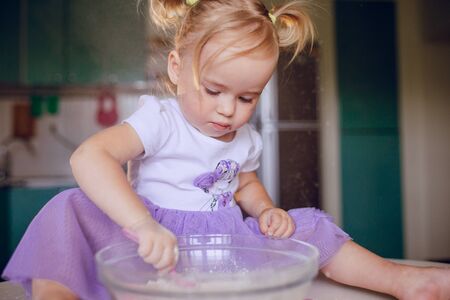 beautiful little girl learns to cook a meal in the kitchenの写真素材