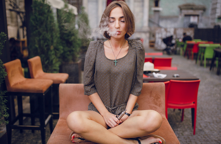beautiful brunette smoke electronic cigarette on the summer terrace of restaurantの写真素材