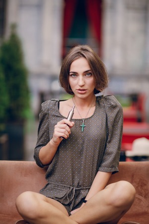 beautiful brunette smoke electronic cigarette on the summer terrace of restaurantの写真素材