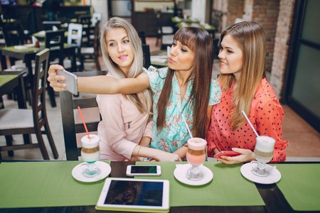 Three beautiful girls in cafes new gadgets are photographed and show photoの写真素材