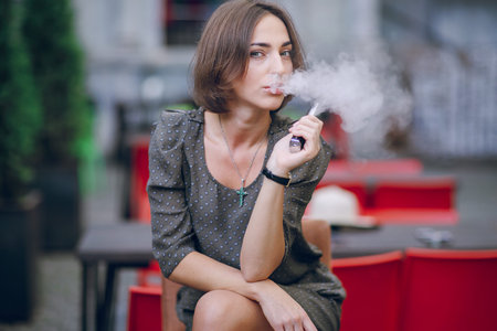beautiful brunette smoke electronic cigarette on the summer terrace of restaurant