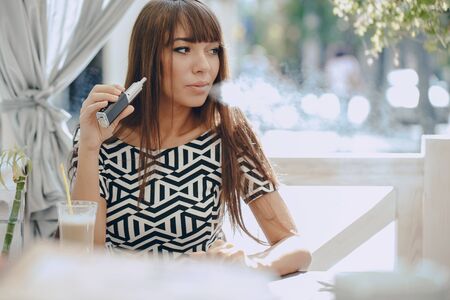 beautiful brunette smoke electronic cigarette on the summer terrace of restaurantの写真素材