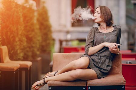 beautiful brunette smoke electronic cigarette on the summer terrace of restaurantの写真素材