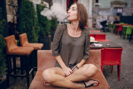 beautiful brunette smoke electronic cigarette on the summer terrace of restaurantの写真素材