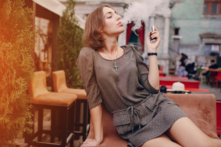 beautiful brunette smoke electronic cigarette on the summer terrace of restaurantの写真素材