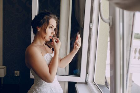 bride paints lips with lipstick on their wedding day in dressの写真素材