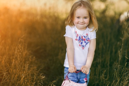 beautiful little girl in the meadow near tree posing and smilingの写真素材