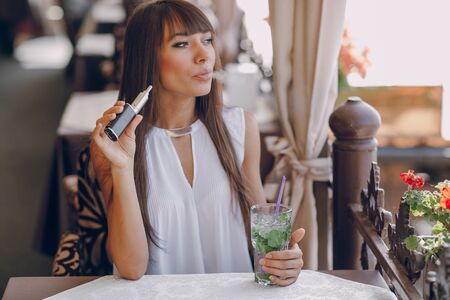 beautiful brunette smoke electronic cigarette on the summer terrace of restaurantの写真素材