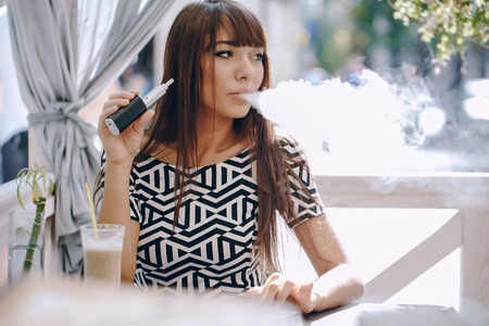 beautiful brunette smoke electronic cigarette on the summer terrace of restaurantの写真素材