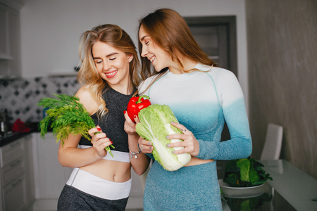 Two sports girl in a kitchen with vegetablesの写真素材
