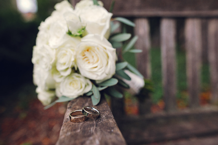 Beautiful wedding bouquet of flowers. White roses on a woodden bench. Two gold ringsの写真素材