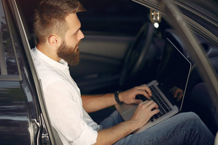 Stylish businessman sitting in a car and use the laptop