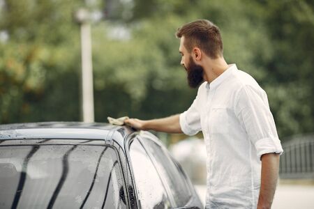 Man in a white shirt wipes a car in a car washの写真素材