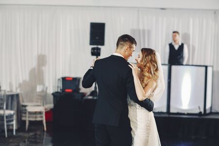 Beautiful bride in a long white dress. Handsome fiance in a blue suit. Couple dance the first wedding danceの写真素材