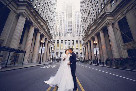 Elegant bride in a white dress and veil. Handsome groom in a blue suit. Couple in a big cityの写真素材