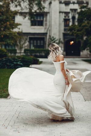 Beautiful bride in a long white dress. Woman with bouquet of flowers. Lady dancing in a parkの写真素材
