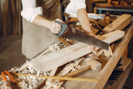 Man working with a wood. Carpenter in a white shirt. Worker with a sawの写真素材