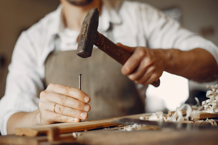 Man working with a wood. Carpenter in a white shirt. Man hammering nails into the wood