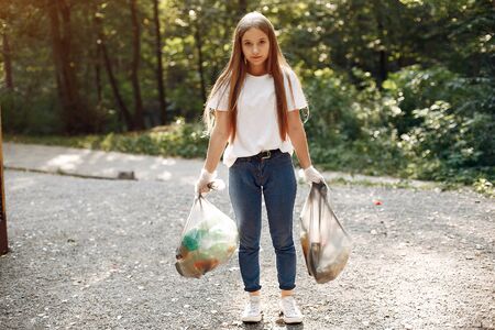 Girl collects garbage in garbage bags in parkの写真素材
