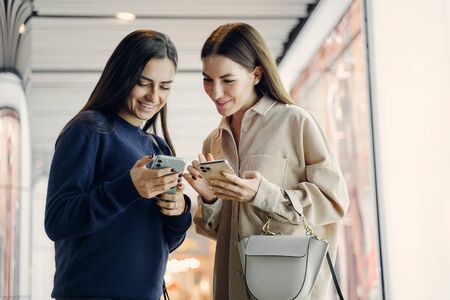 two girlfriends using their cellphone while exploring a new city at nightの写真素材