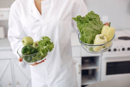 Healthy eating. Dieting and people concept. Brunette with a vegetable. Doctor in uniformの写真素材