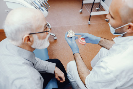 Handsome old man talking to the dendist. Two men in the dentist's office. The doctor shows the...