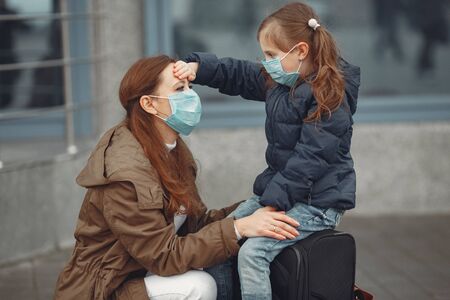 European mothers in respirators with kids are standing near a building.の写真素材