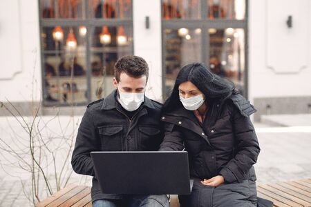 People in a masks sitting in a city with a laptopの写真素材