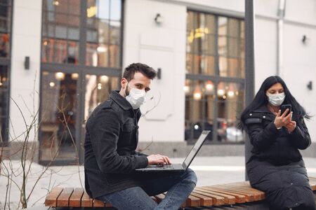 People in a masks sitting in a city with a laptopの写真素材