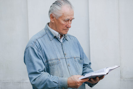 Elegant old man standing on gray background with a book
