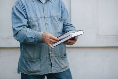 Elegant old man standing on gray background with a bookの写真素材
