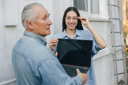 Girl teaching her grandfather how to use a laptopの写真素材