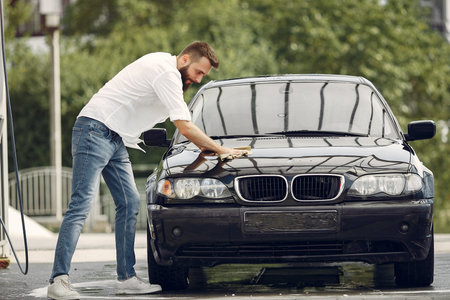 Man in a white shirt wipes a car in a car wash