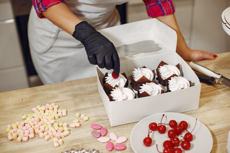 Confectioner in a kitchen. Woman in a uniform. Professional decorates the cakes.