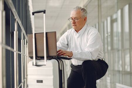 Elegant old man at the airport with a suitcaseの写真素材